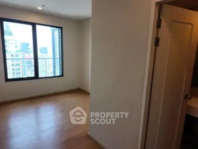 Spacious empty room with large window and wooden flooring in modern apartment.