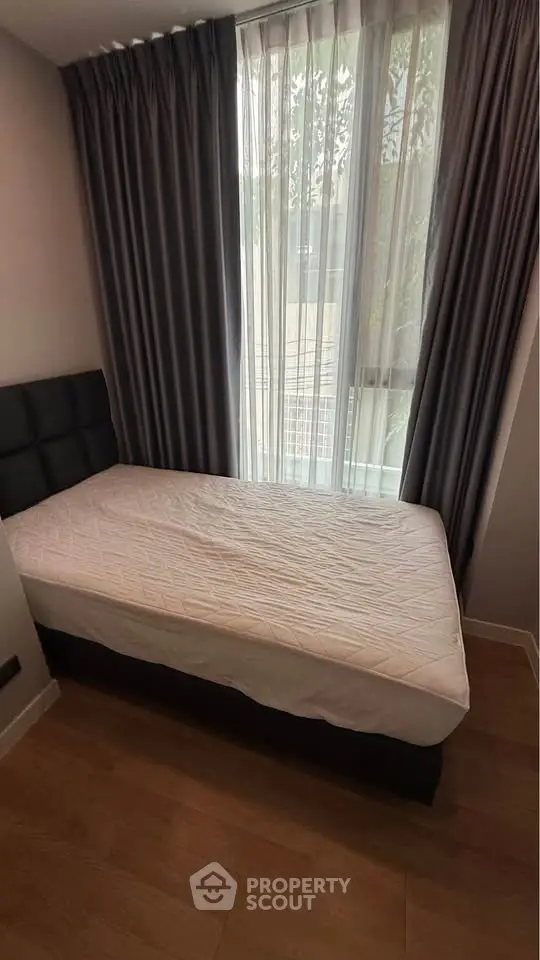 Cozy bedroom with a single bed and floor-to-ceiling window with curtains, offering natural light and comfort.