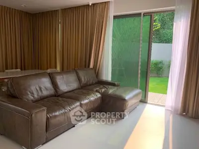 Spacious living room with leather sofa and garden view, perfect for relaxation and entertaining.