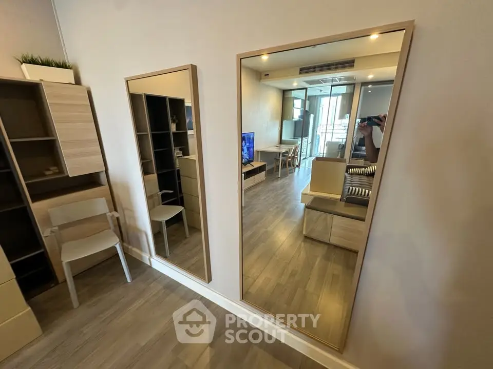 Modern living room with wooden flooring and stylish furniture, featuring a large mirror and open layout.