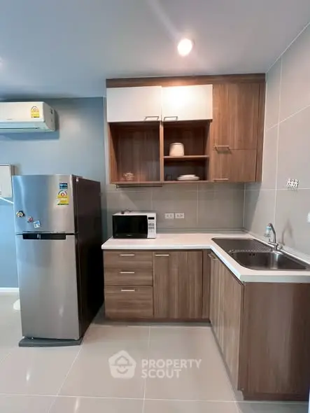 Modern kitchen with sleek wooden cabinets, stainless steel fridge, and microwave in a stylish apartment.