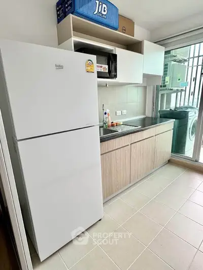 Modern kitchen with sleek cabinets, fridge, and washing machine in a bright, compact space.