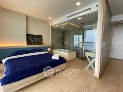Modern bedroom with glass-enclosed bathroom and wooden flooring, featuring a cozy bed and contemporary design.