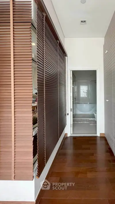 Modern hallway with wooden flooring leading to a sleek bathroom with glass shower enclosure.