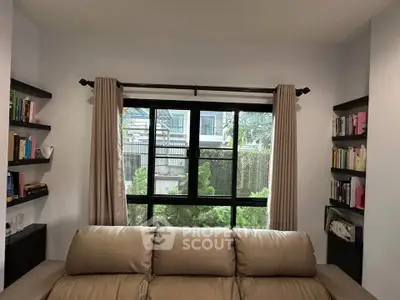 Cozy living room with large window and bookshelves, offering a serene garden view.