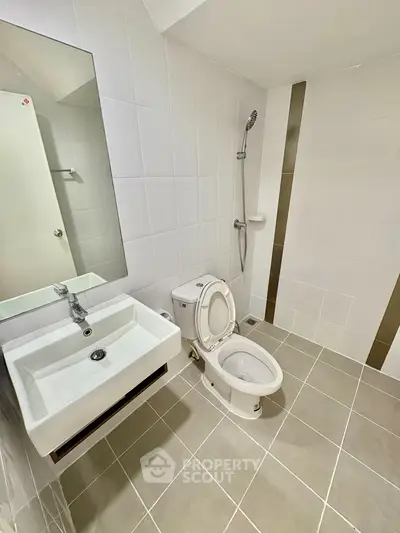 Modern bathroom with sleek fixtures and neutral tiles, featuring a toilet, sink, and shower area.