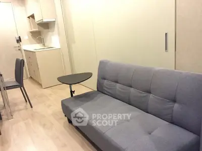 Modern studio apartment with sleek kitchen and cozy living area featuring a stylish gray sofa.