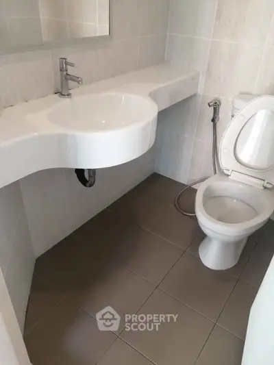 Modern bathroom with sleek white fixtures and tiled walls, featuring a contemporary sink and toilet.