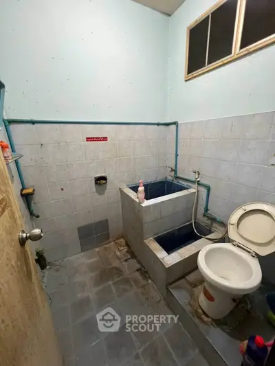 Compact bathroom with tiled walls and floor, featuring a toilet and a traditional bathing area.