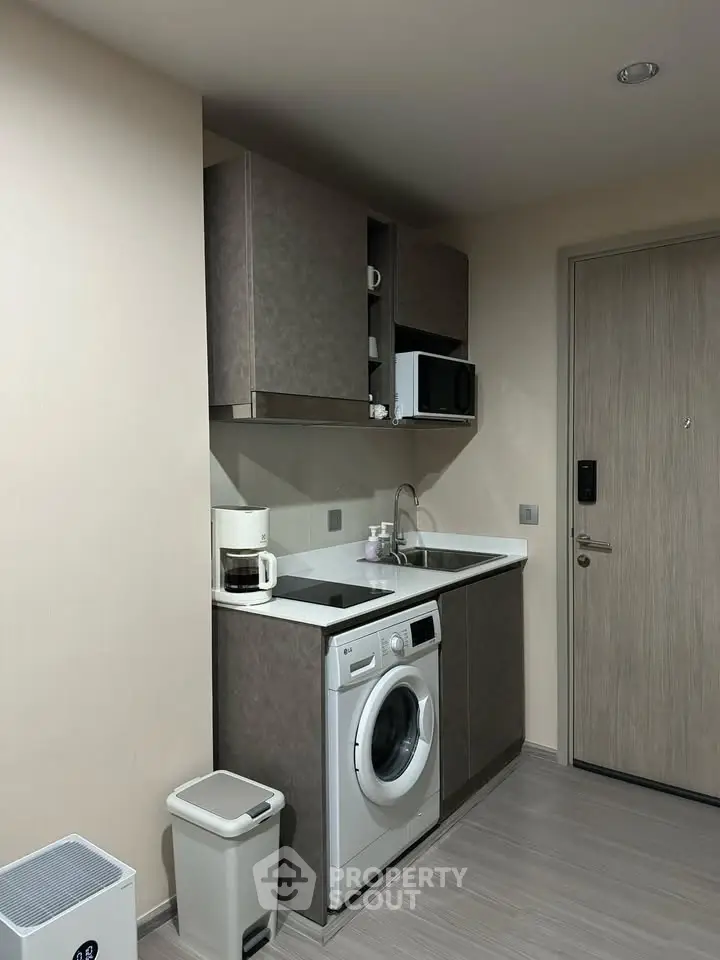 Compact modern kitchen with washing machine and microwave in sleek apartment.