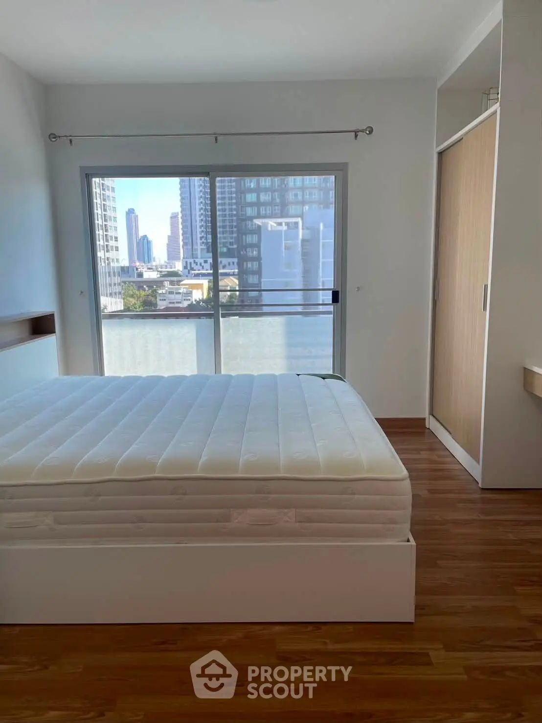 Modern bedroom with city view, featuring a large window and sleek wooden flooring.