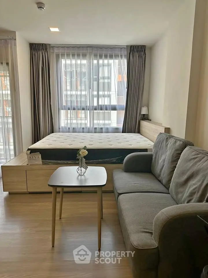 Modern studio apartment with cozy bed and stylish sofa, featuring large windows for natural light.