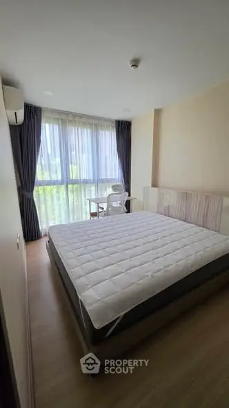Spacious bedroom with large window and modern furnishings in a bright apartment.