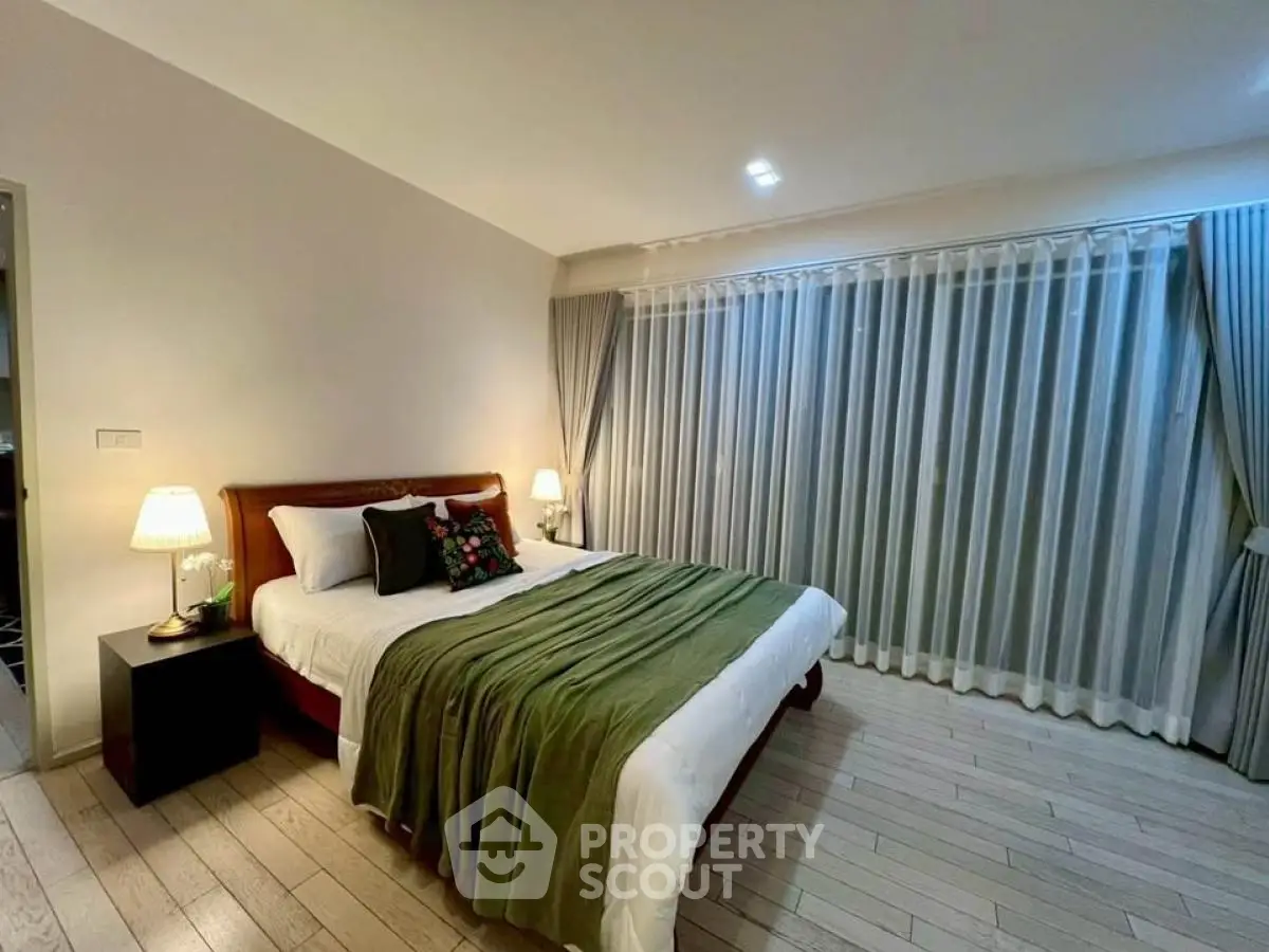 Spacious bedroom with elegant decor and large window drapes in modern apartment.