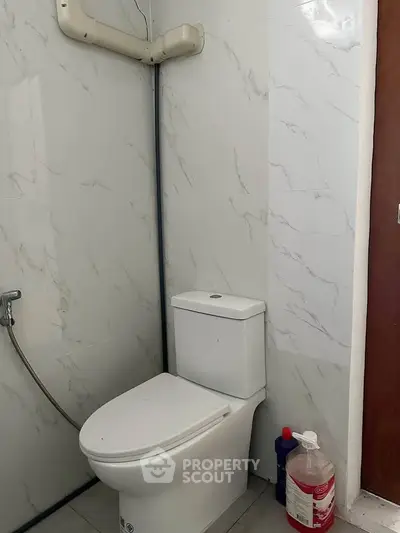 Modern bathroom with sleek white toilet and marble wall tiles, featuring a handheld bidet spray.
