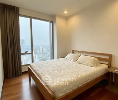Modern bedroom with city view, featuring a wooden bed frame and large window for natural light.