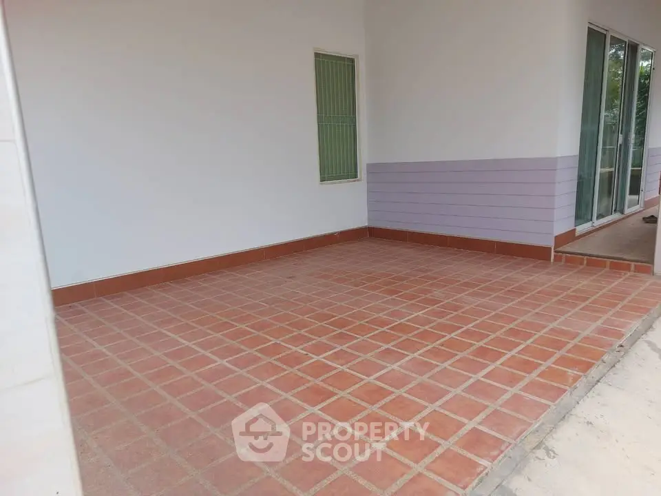 Spacious tiled patio with sliding glass doors and window, ideal for outdoor relaxation.