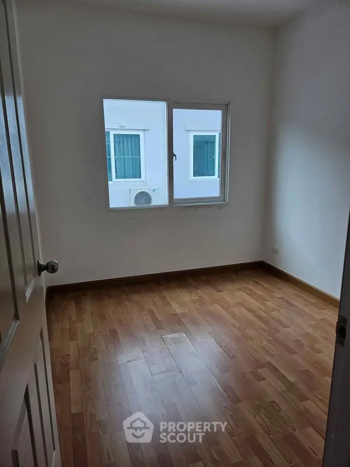 Spacious empty room with wooden flooring and window view, perfect for customization.