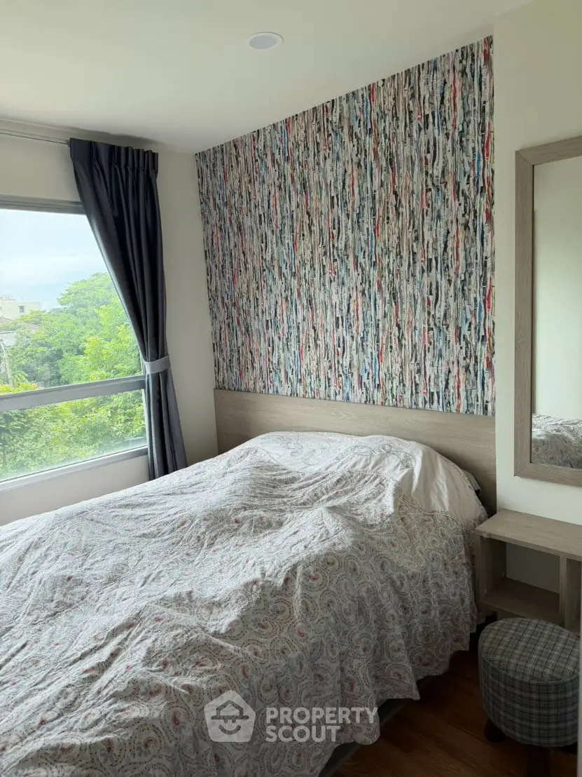 Cozy bedroom with colorful accent wall and large window with green view.