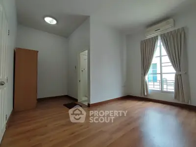 Spacious bedroom with wooden flooring and large window, featuring an air conditioner and wardrobe.