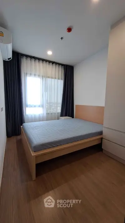 Modern bedroom with wooden flooring and large window offering natural light