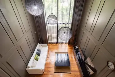 Luxurious high-ceiling living room with modern decor and large windows offering natural light and greenery views.