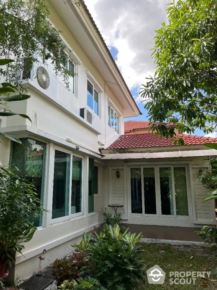 Charming two-story home with terracotta roof tiles and lush greenery, featuring expansive windows and a serene garden space.