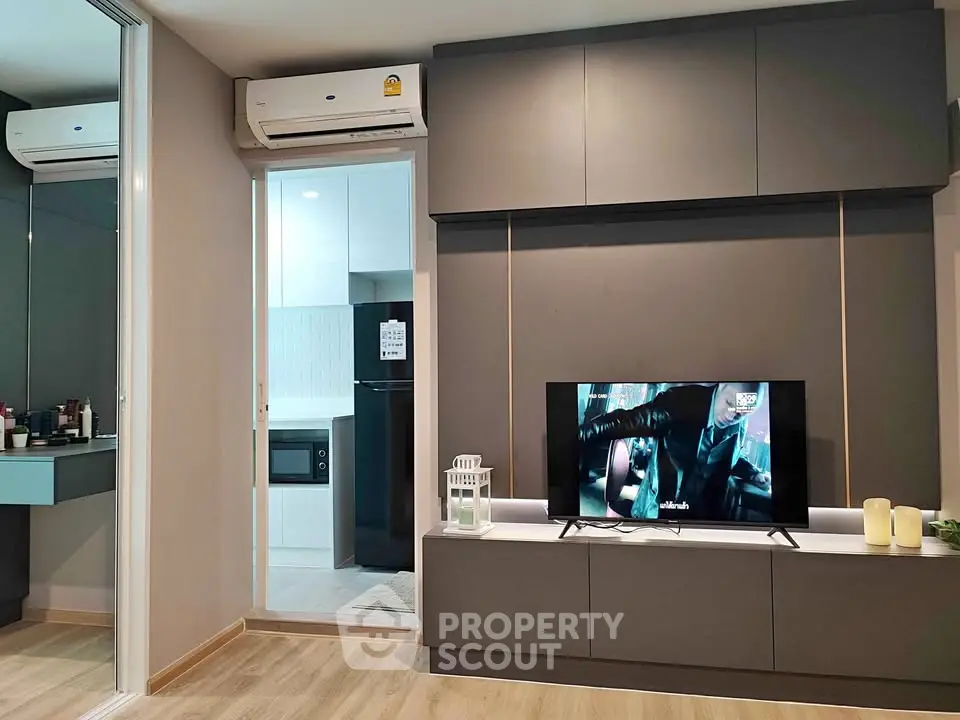 Modern living room with sleek design, featuring built-in TV unit and air conditioning, adjacent to a compact kitchen.