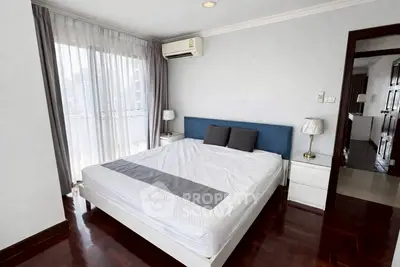 Spacious bedroom with large window and modern furnishings in a city apartment.