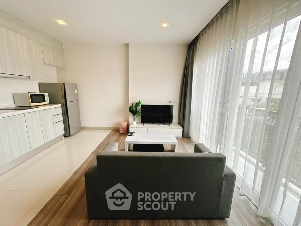 Modern living room with open kitchen, sleek furniture, and large windows for natural light.