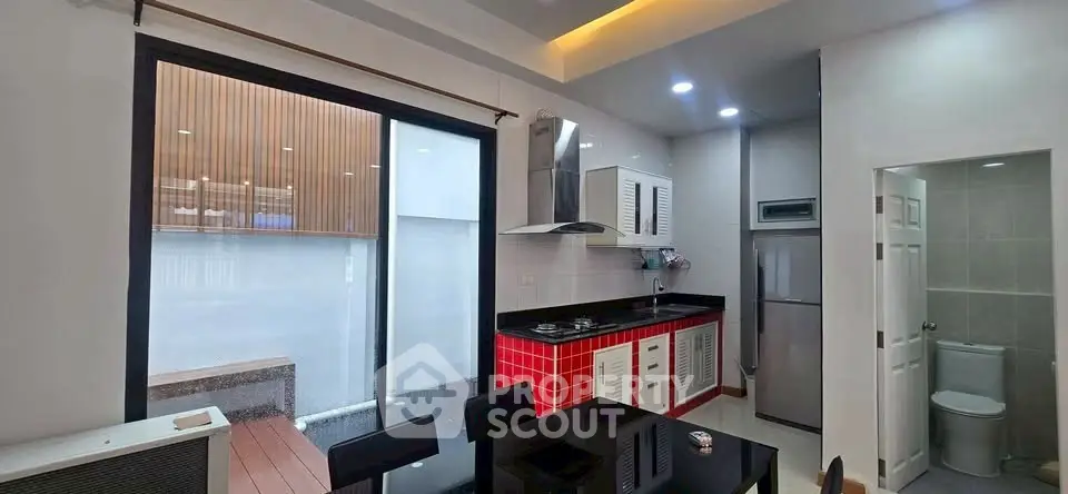 Modern kitchen with red cabinetry and open layout, adjacent to a small outdoor space.