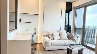 Modern living room with cozy sofa, sleek desk, and large windows offering stunning city views.