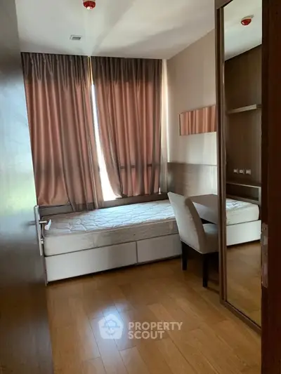 Cozy bedroom with wooden flooring and large window, featuring a single bed and a study desk.