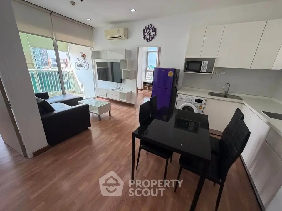 Modern open-plan living room with kitchen, featuring sleek furniture and city view balcony.