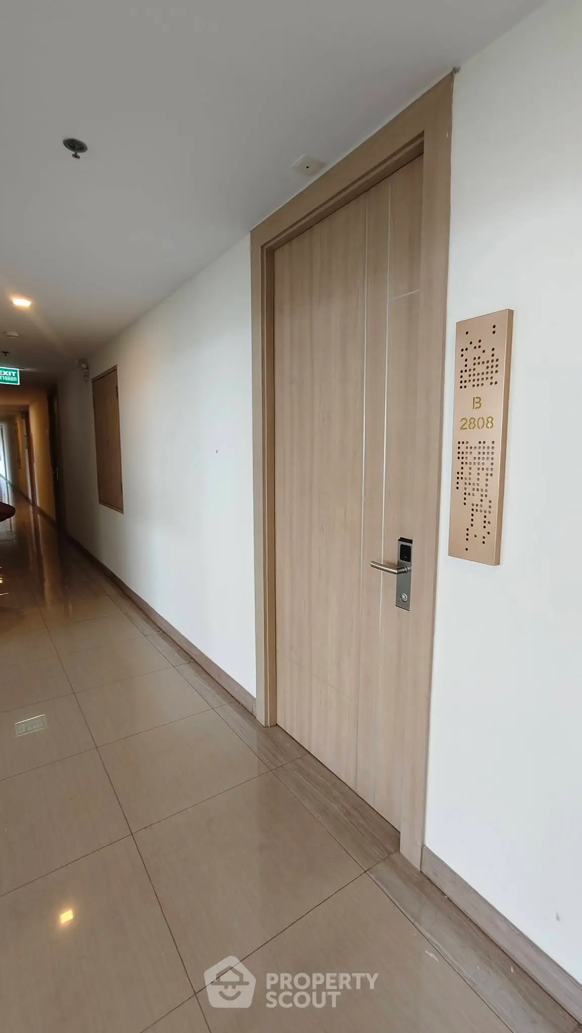 Modern apartment corridor with sleek wooden door and polished tile flooring.