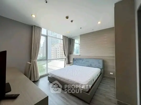Spacious modern bedroom with large windows and city view, featuring elegant decor and natural light.
