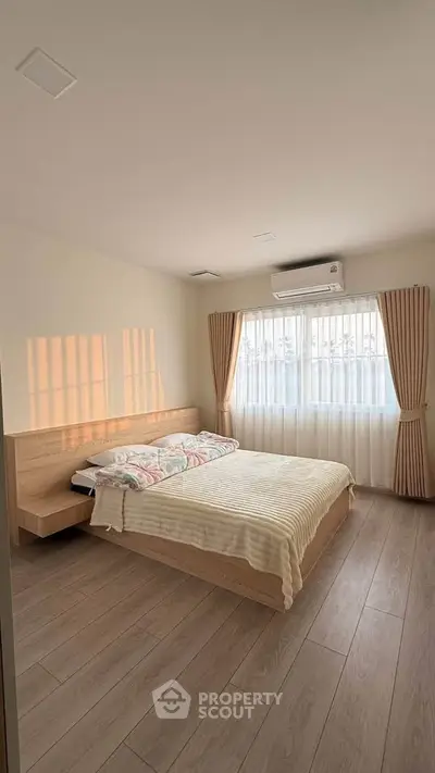 Spacious bedroom with natural light, wooden flooring, and modern air conditioning unit.