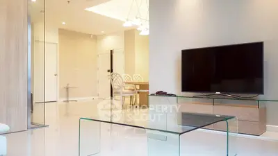 Modern living room with glass coffee table and flat-screen TV, elegant dining area in background.