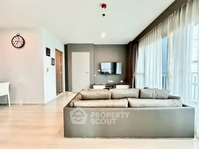 Modern living room with sleek sofa and wall-mounted TV, featuring large windows and stylish decor.