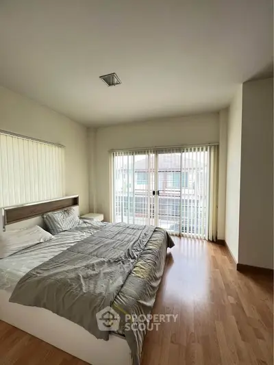 Spacious bedroom with large windows and wooden flooring in modern apartment.