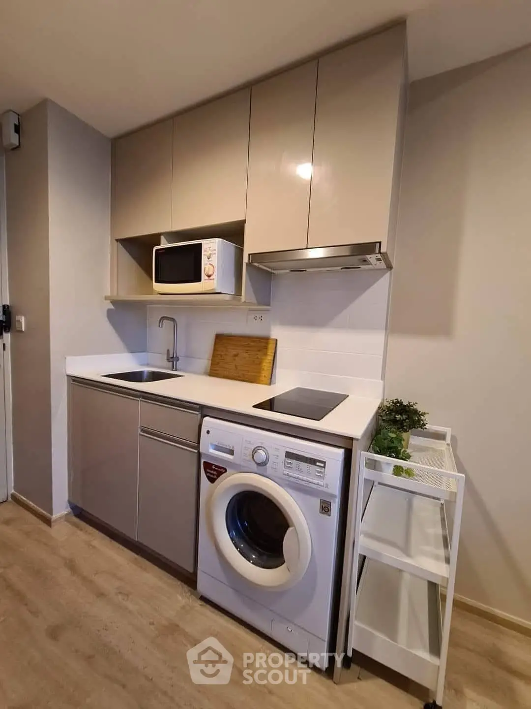 Modern compact kitchen with washing machine and microwave, sleek cabinetry, and wooden flooring.