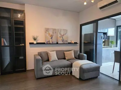 Modern living room with cozy gray sofa and stylish decor, adjacent to sleek kitchen with glass partition.