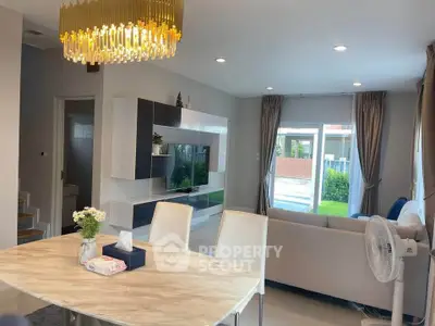 Modern living room with elegant chandelier and stylish furniture, featuring a large window view.