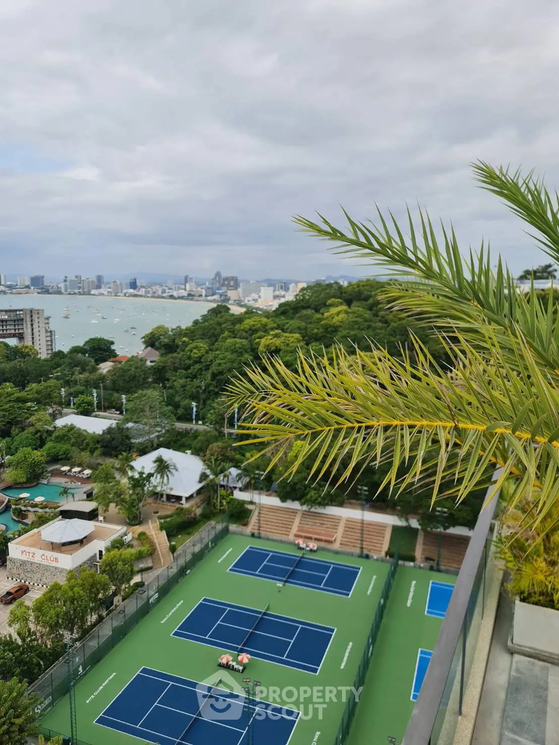 Stunning aerial view of tennis courts with lush greenery and ocean backdrop, perfect for luxury living.