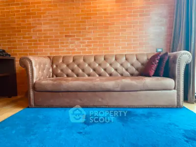 Luxurious brown leather sofa in stylish living room with brick wall and blue carpet