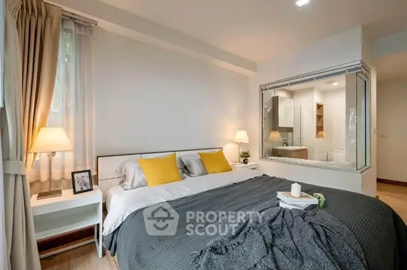 Modern bedroom with cozy lighting and large window, featuring a unique glass partition to the bathroom.