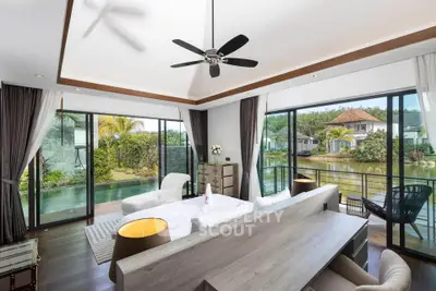 Luxurious living room with panoramic garden and water views, featuring modern decor and ceiling fan.