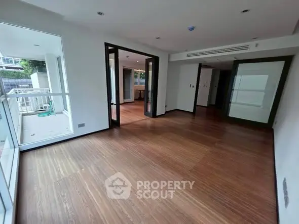 Spacious modern living room with wooden flooring and large windows for natural light.