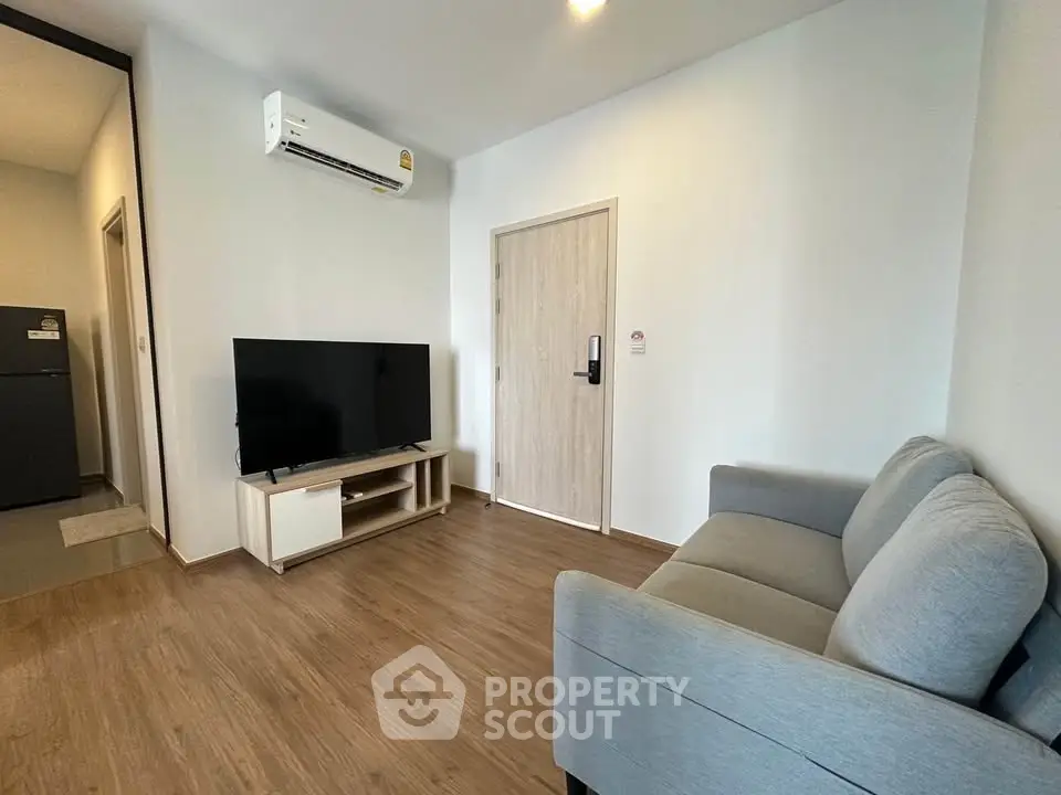 Modern living room with sleek design, featuring a comfortable sofa, flat-screen TV, and air conditioning.