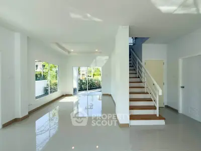 Spacious modern living room with large windows and elegant staircase in a bright, open layout.